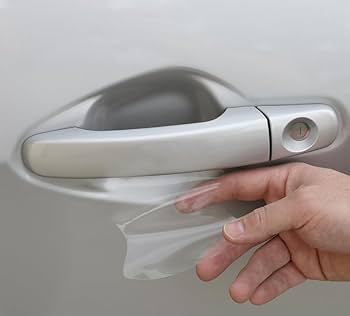 A person engaged in Paint Protection Film Training carefully applies a transparent protective film to a car door handle to prevent scratches.