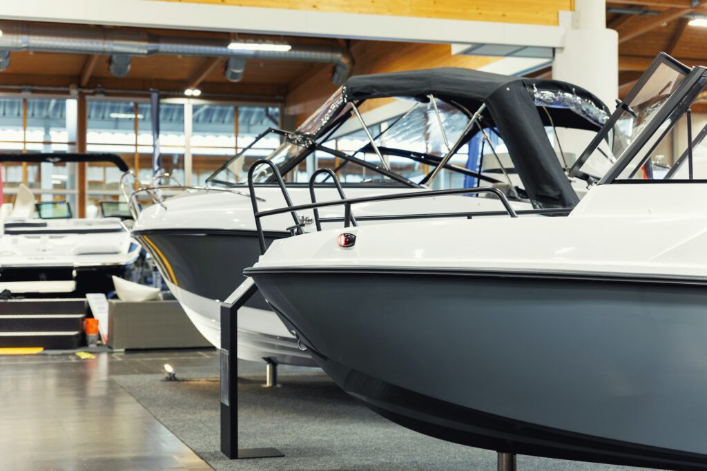 Several motorboats on display indoors at a boat showroom, featuring sleek white and gray exteriors with black canopies, highlight the importance of Paint Protection Film Training to maintain their pristine condition.