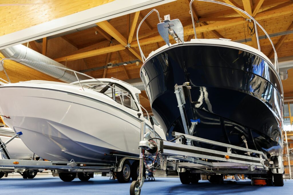 Two boats are displayed in a showroom, one white and one black, both mounted on trailers. The space, perfect for Paint Protection Film Training sessions, has a wooden ceiling and modern lighting.