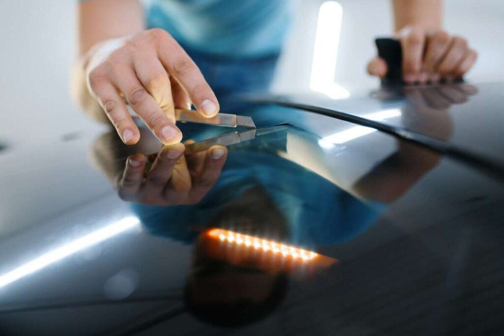 A person uses a metal tool to skillfully repair a dent on a car's surface, ensuring the surrounding PPF remains pristine and undisturbed.