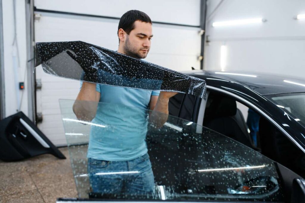 A man expertly applies window tint film to a car door in a garage, complementing the precision used for PPF windshield protection film.