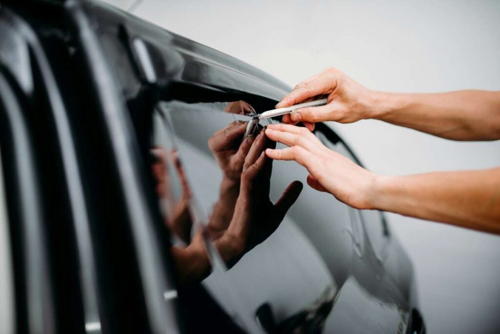 Hands skillfully applying tint film to a car window with a precision tool, ensuring the highest quality of PPF windshield protection film.