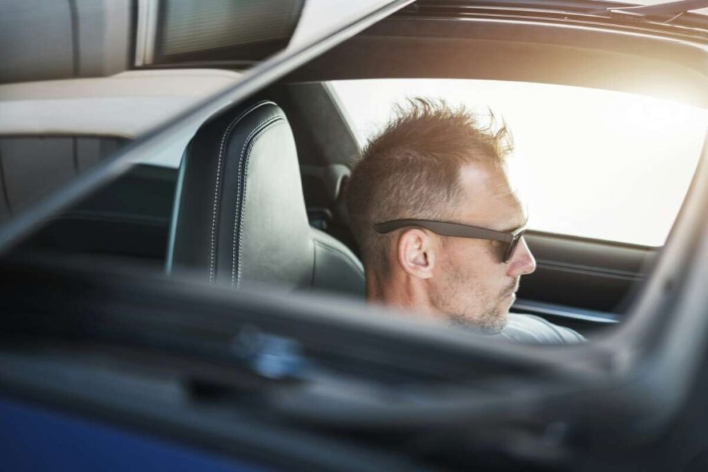 A man wearing sunglasses sits in a car with the sunroof open, enjoying the view from the side. The sleek vehicle features PPF ceramic window tint, enhancing both privacy and style.