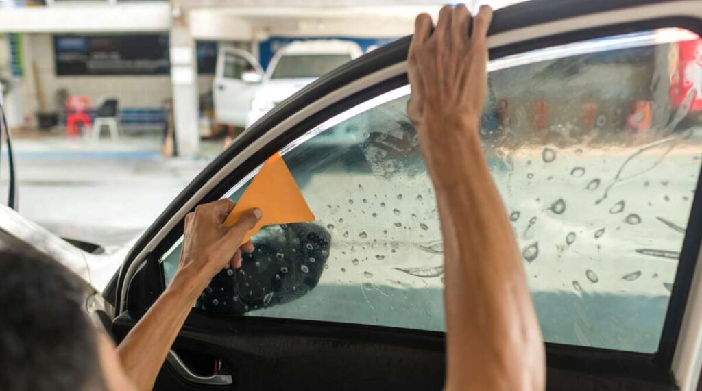 Applying PPF windshield protection film, the person carefully uses an orange squeegee to ensure the tinted film adheres perfectly to the car window.