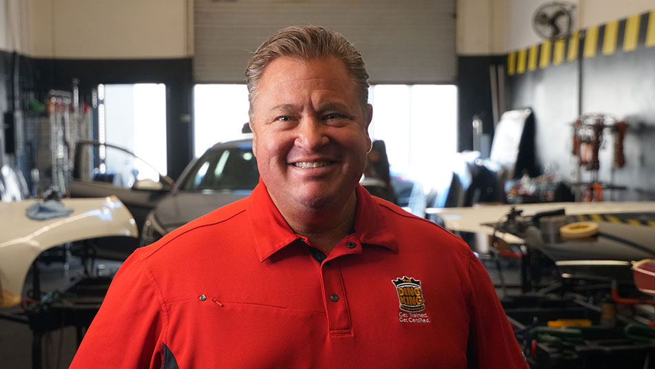A man in a red shirt standing in a garage, specializing in Paintless Dent Repair.