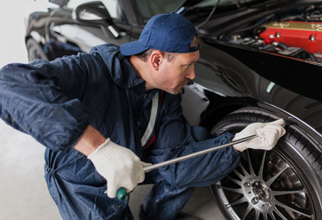 A certified mechanic is conducting paintless dent repair on a car in a garage.