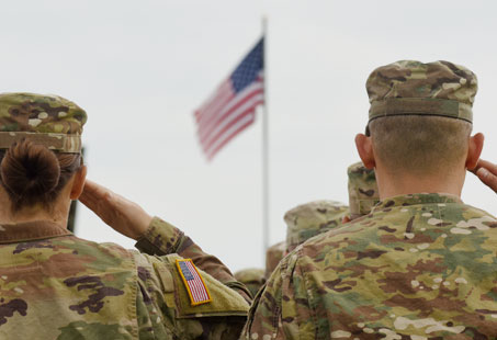 A group of soldiers saluting an american flag during a patriotic ceremony.