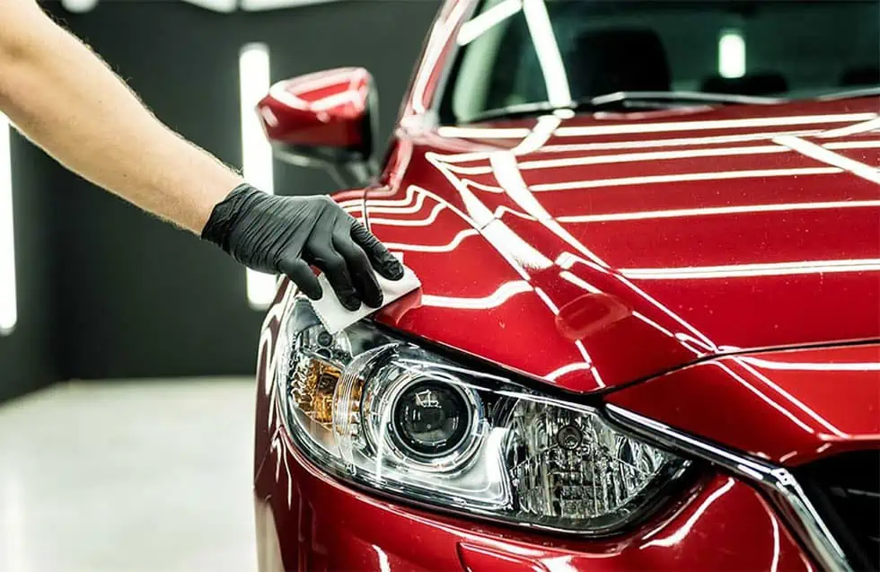 A person is polishing the hood of a red car to apply ceramic coating.