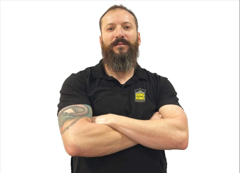 A bearded man wearing a black shirt with his arms crossed.