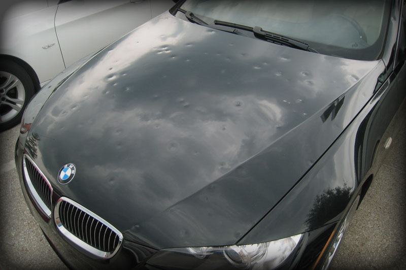 The hood of the black car beneath a cloudy sky.