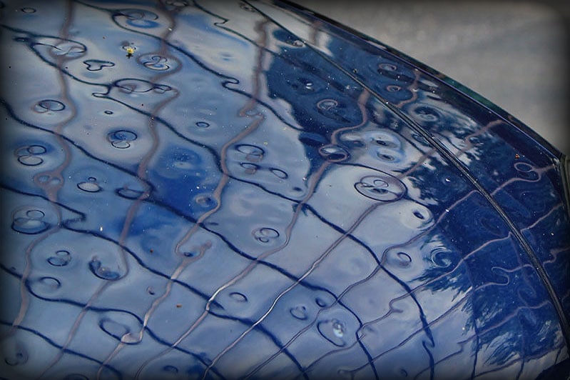 A close up of a blue car with water droplets on it at the Colorado Hail Repair School.