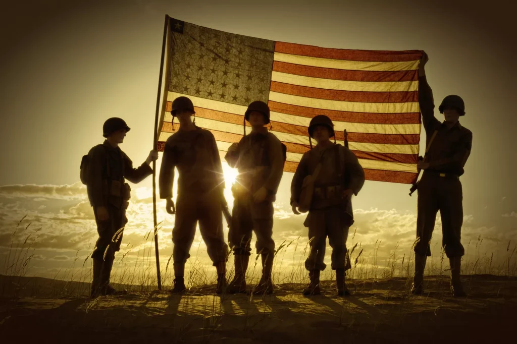 Five soldiers, silhouetted against a breathtaking sunset, hold a large American flag. These veterans exemplify bravery and dedication, standing together as symbols of vocational rehabilitation and resilience.