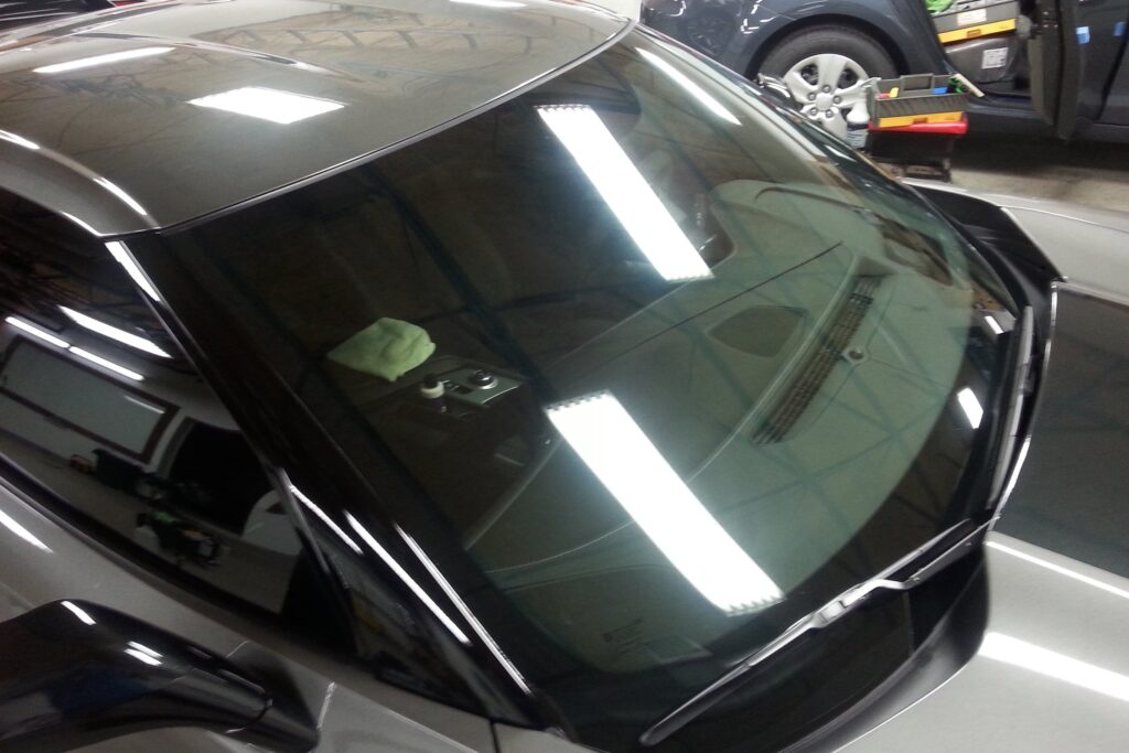 A car with a clean windshield reflecting ceiling lights, showcasing the well-preserved interior dashboard through the glass, thanks to our comprehensive Paint Protection Film Training.